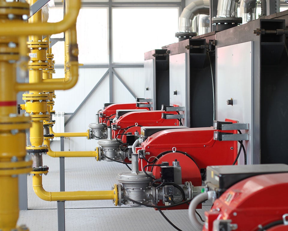 Industrial gas burner system with red units and yellow pipes in a technical facility.