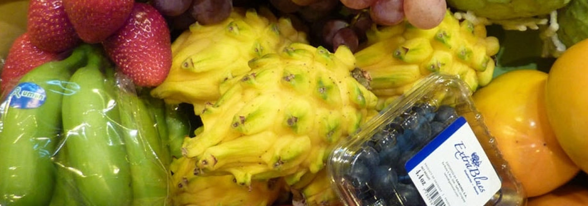 Variedad de frutas como uvas, fresas, pitayas amarillas, guanábanas, mangos, granadas, bananos y arándanos en un arreglo colorido.