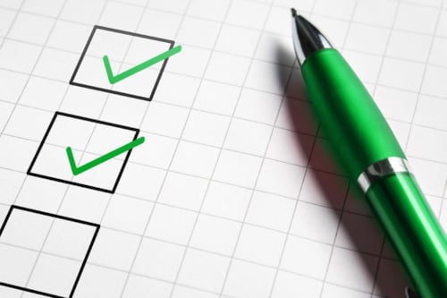 Checklista på ett rutat papper, några är avbockade med grön penna som ligger bredvid på papperet.