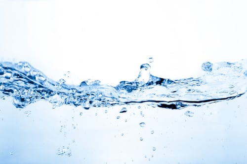 Klar vattenskvätt mot vit bakgrund, med synliga bubblor och rörelse i vätskan.