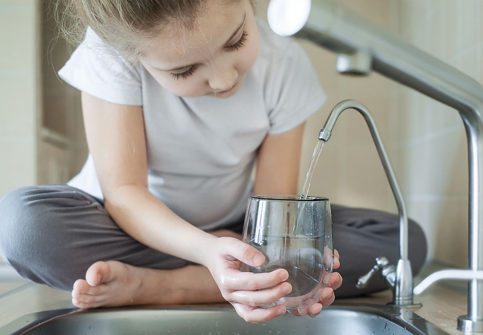 Young girl filling a glass with tap water in the kitchen sink.