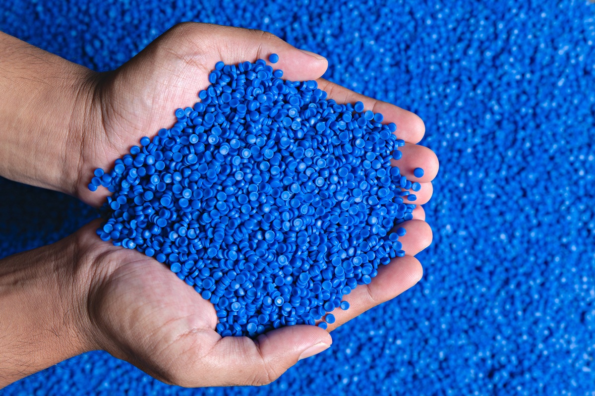 Hands holding a pile of blue plastic pellets against a background of blue granules.