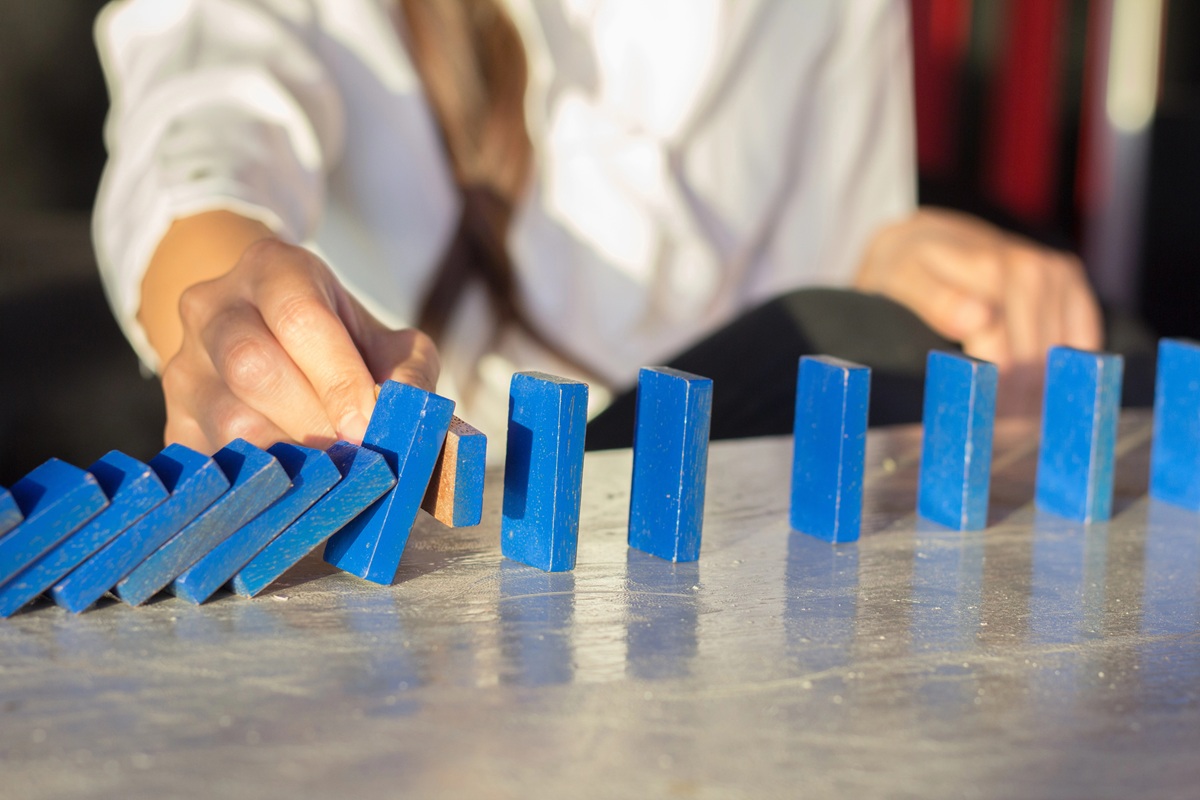 A person in a white shirt topples a blue domino next to a row of standing blue dominoes on a table.