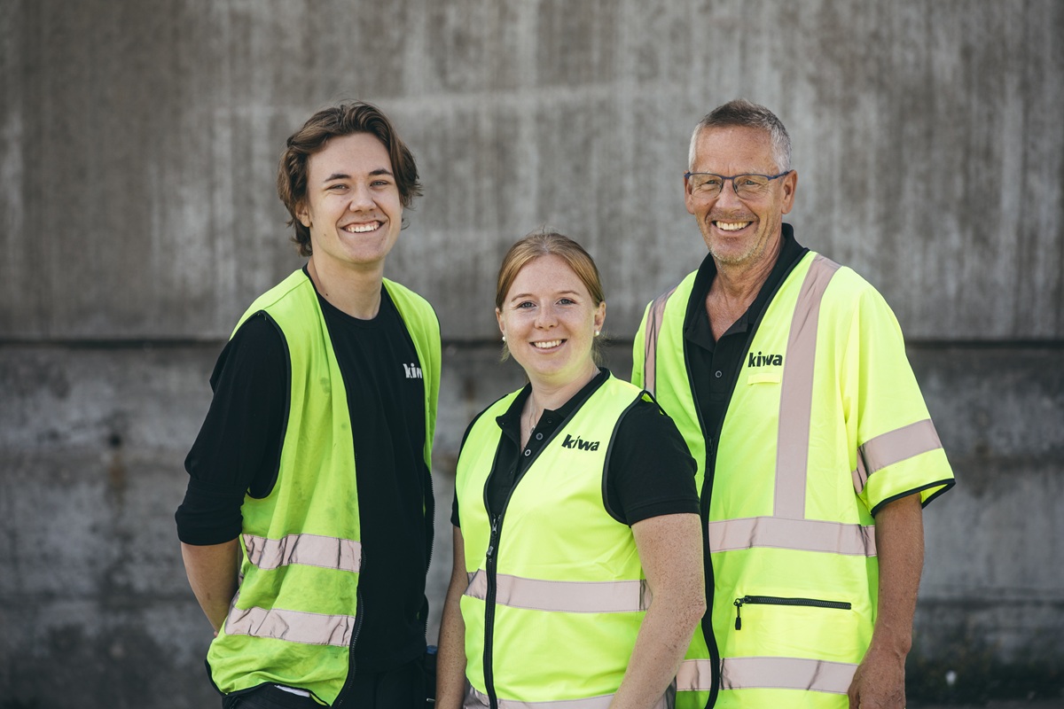 Three people in hi-vis safety vests smiling outdoors, with a concrete background.