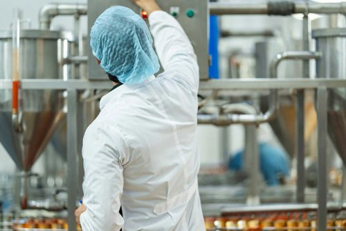 Person i vit skyddsklädsel kontrollerar industriell livsmedelsutrustning i en produktionsanläggning.