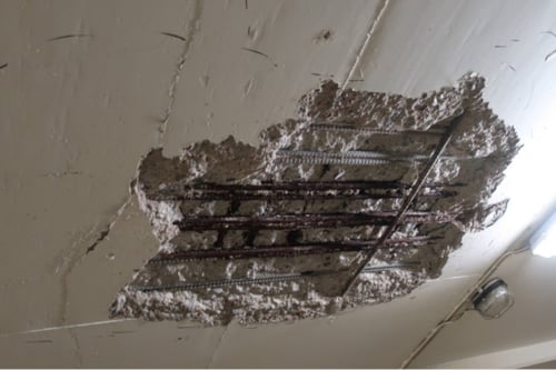 Betongen i ett tak har skadats och blottlagt ett stort hål där även armeringen blivit synlig.