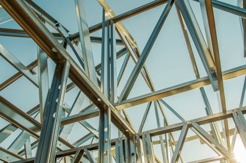 Solen reflekterar mot blänkande stålskelett med blå himmel i bakgrunden.