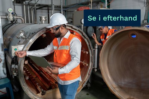Två industriarbetare i skyddsutrustning inspekterar en stor trycktank med laptop i en fabrik.